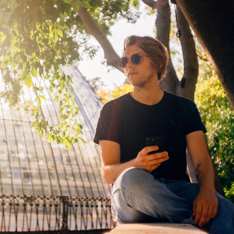 Photograph: Matthew sitting outside in a park in front of a domed greenhouse.