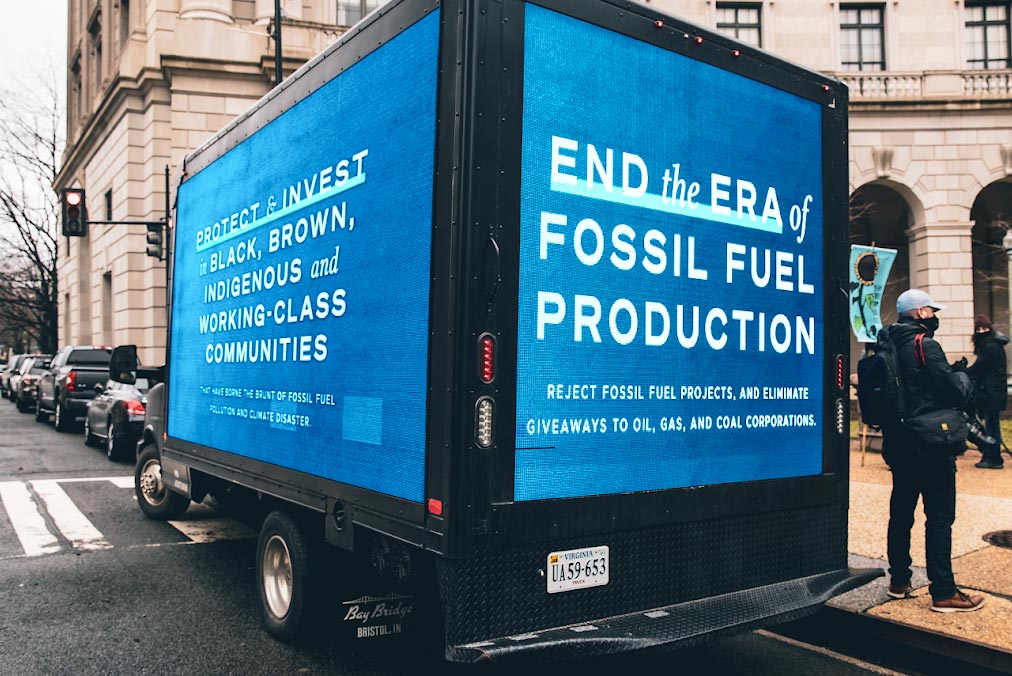 Photo of a box truck with video panels covering the sides and rear. One of the screens reads 'Protext and invest in black, brown, indigenous and working class communities'.