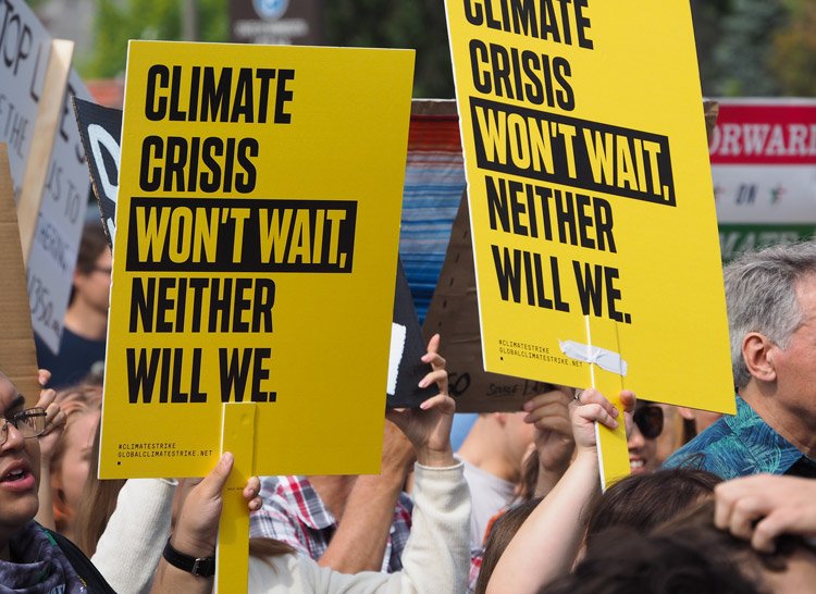 Photo of people at a rally, holding up signs that read 'climate crisis won't wait, neither will we