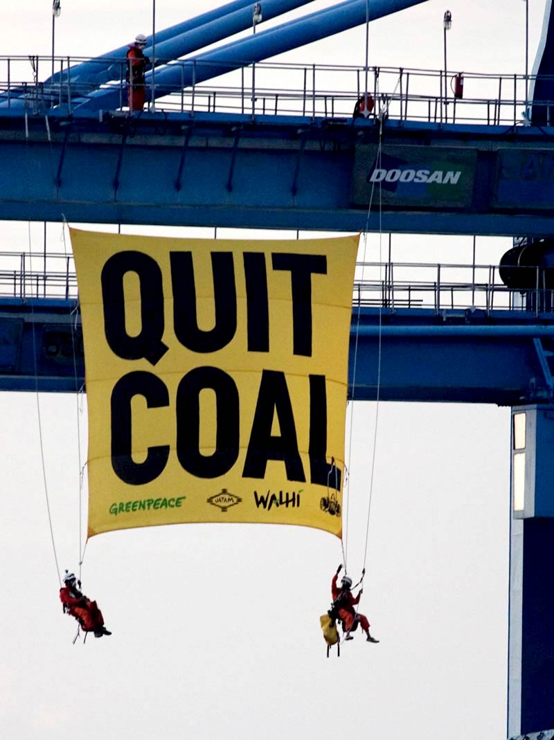 A massive multi-story yellow banner hanging from a coal crane, reading 'Quit Coal'.