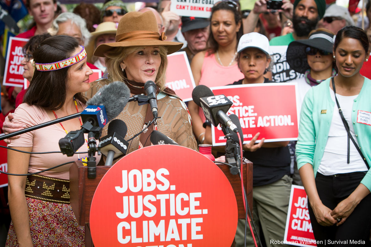 Jane Fonda and Melissa Laboucan-Massimo giving a speech at an outdoor podium labeled 'Jobs, Justice, Climate'.