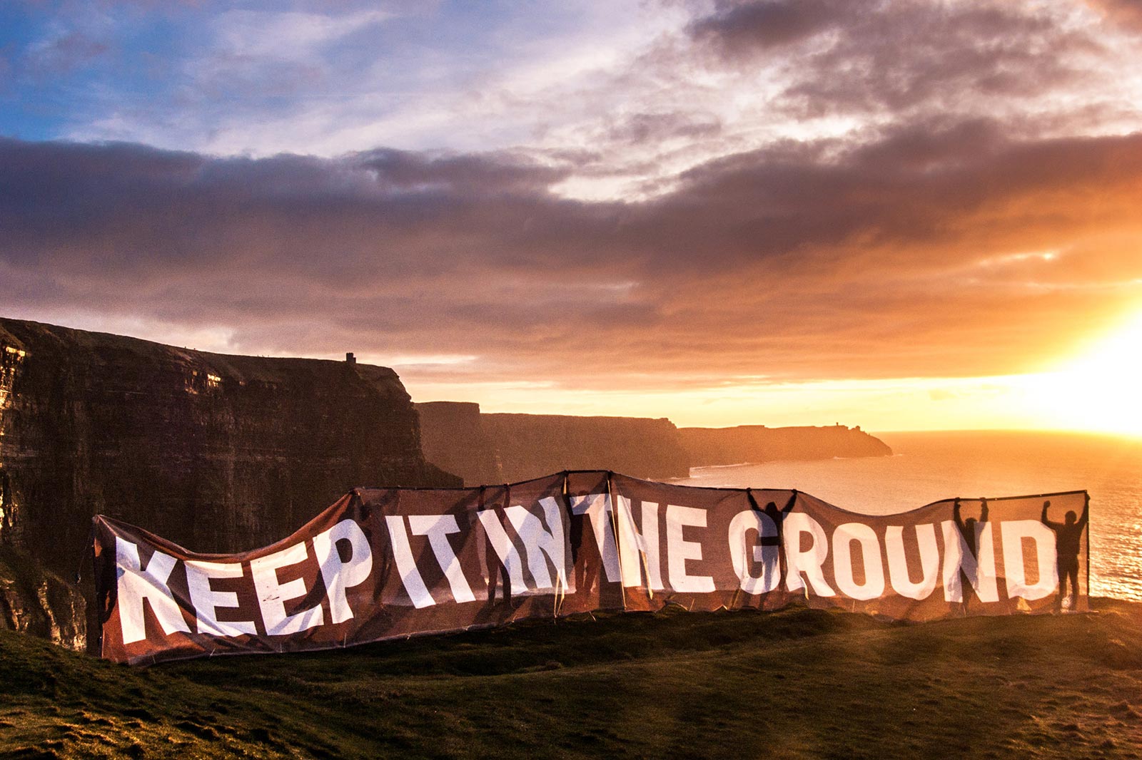 Banner reading 'Keep it in the Ground' being displayed dramatically at the top of the Cliffs of Moher in Ireland.